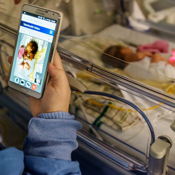 una persona che tiene in mano un telefono con un bambino sullo sfondo