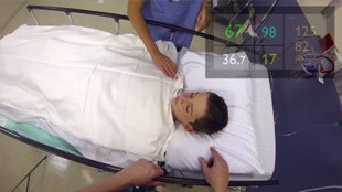 Campo visivo di una persona che indossa i Google Glass – Il paziente è in sala risveglio e i parametri vitali sono visualizzati nell'angolo superiore destro del campo visivo.