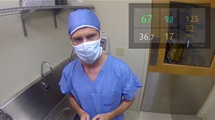Un medico in sala operatoria visualizza i parametri vitali nell'angolo in alto a destra del campo visivo.