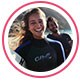 : Immagine del profilo dell’utente, una giovane donna in muta che sorride su una spiaggia ventosa.