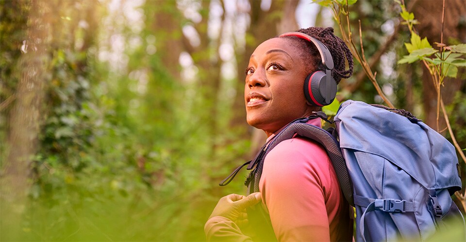 Donna che cammina in una foresta con uno zaino blu, indossa le cuffie Philips A6219 e alza lo sguardo con un sorriso