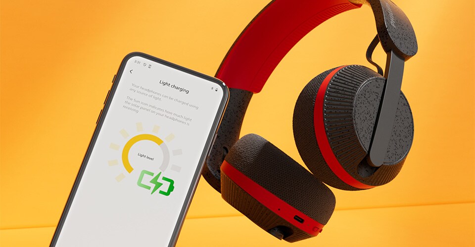 Cuffie Philips A6219 accanto a uno smartphone che mostra la schermata di ricarica luminosa, su uno sfondo arancione brillante