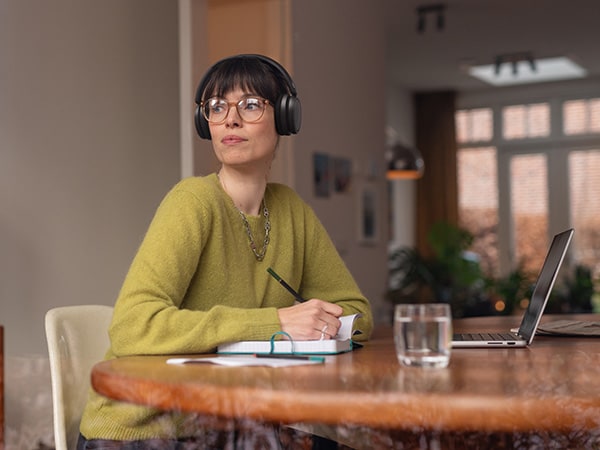 Una persona con auricolari Philips comodi è seduta a un tavolo con un quaderno e un laptop