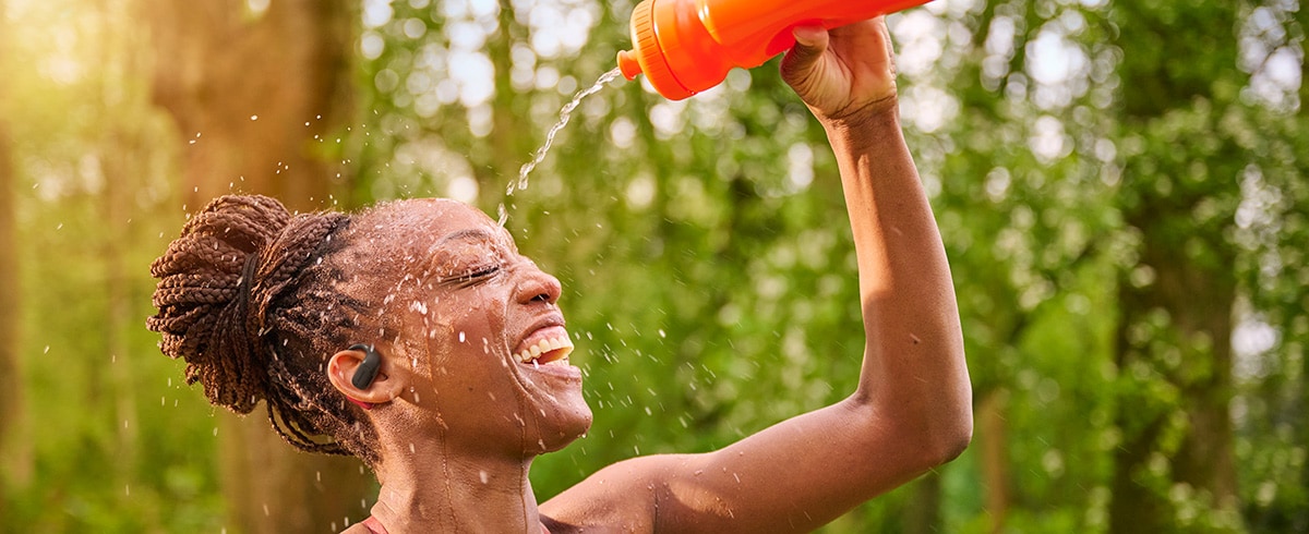 Donna che si rinfresca versandosi acqua sulla testa mentre indossa le cuffie sportive Philips all'aperto