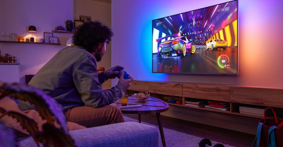  Una persona è seduta su un divano e gioca a un videogioco di corse su una TV Philips Ambilight