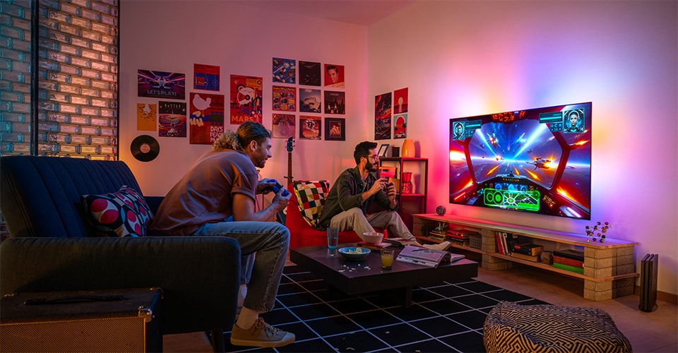 Due persone giocano con entusiasmo a un videogioco a tema spaziale in un accogliente e colorato soggiorno
