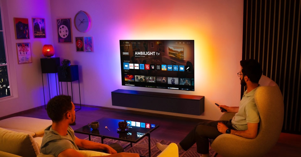 Due uomini guardano una TV Ambilight montata a parete in un soggiorno