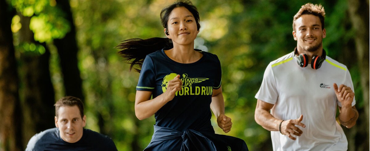 Tre partecipanti alla Wings for Life World Run corrono felici, indossando le cuffie sportive Philips.