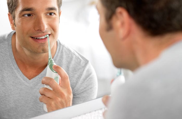 Un uomo guarda il proprio riflesso mentre si lava i denti bianchi con uno spazzolino elettrico.