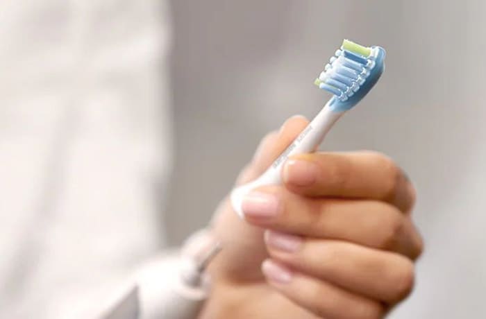 : Primo piano della mano di una persona che sta applicando la testina removibile su uno spazzolino elettrico bianco.