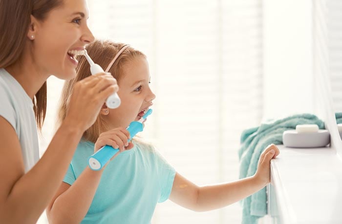 Una bambina e sua madre si stanno lavando i denti bianchi con degli spazzolini elettrici.