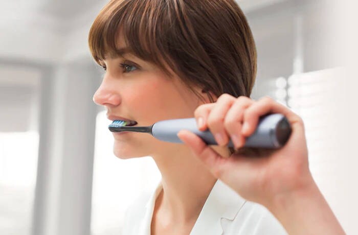 Giovane donna dai capelli scuri che si lava i denti con uno spazzolino elettrico Philips Sonicare.