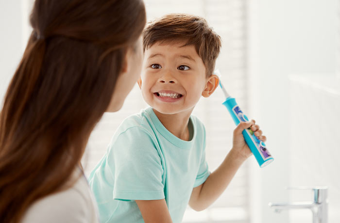 un bambino sorride a sua madre mentre tiene in mano uno spazzolino Philips Sonicare for Kids blu.