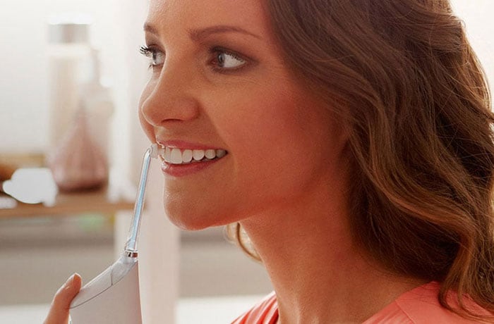 Una donna si lava i denti bianco perla con lo spazzolino elettrico Philips Sonicare Airfloss.