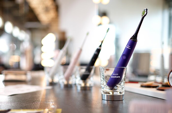 Spazzolini elettrici Philips Sonicare blu, neri, rosa e bianchi in fila in bicchieri trasparenti.