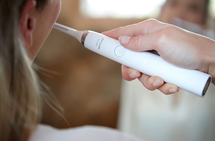 Primo piano di una donna che si lava i denti con uno spazzolino elettrico Philips Sonicare bianco.