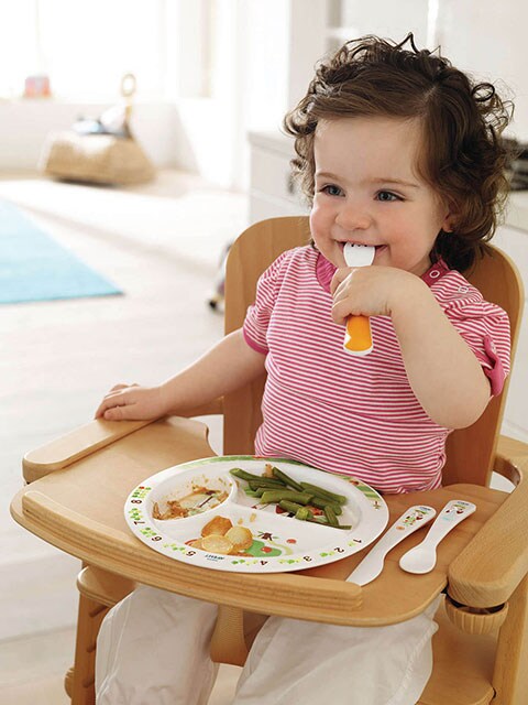 Bimba seduta sul seggiolone mentre mangia con il suo set pappa colorato