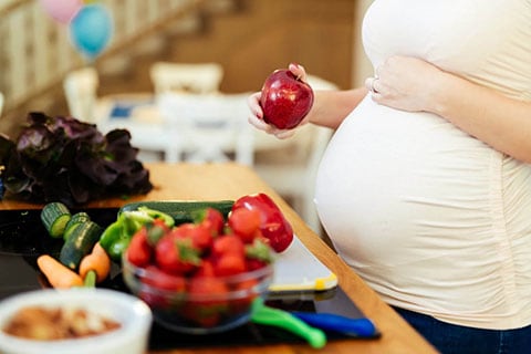 Mamma con il pancione vicino a un buffet di frutta e verdura