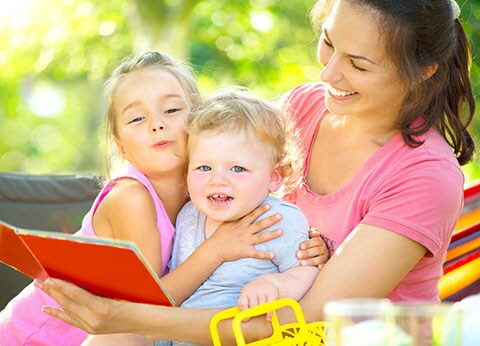 Giovane mamme sorridente che legge un libro ai suoi due bambini