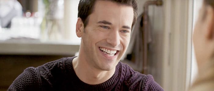 Primo piano di un uomo sorridente e ben rasato con un maglione scuro
