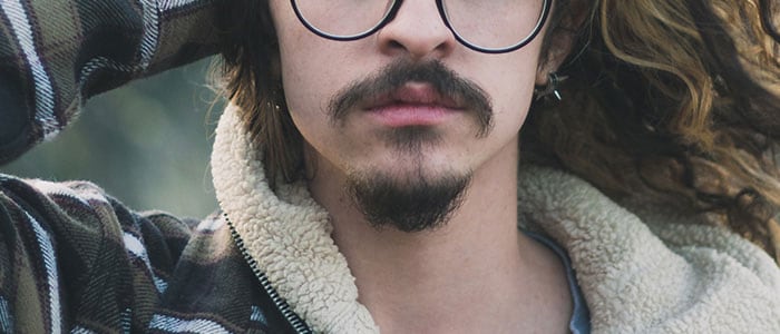 Primo piano del mento di un uomo con lunghi capelli ondulati e baffi da moschettiere con pizzetto.