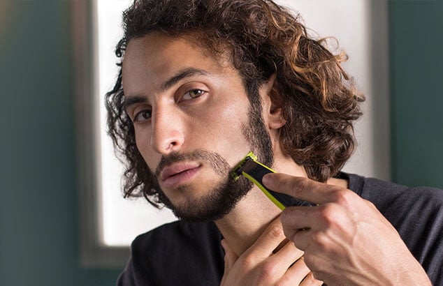 Un uomo si sta radendo una zona della barba dall’alto verso basso, iniziando a modellare un pizzetto.