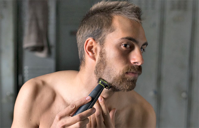 Un uomo sta tagliando la sua barba trasandata per fare una barba corta usando un rasoio con un accessorio speciale.