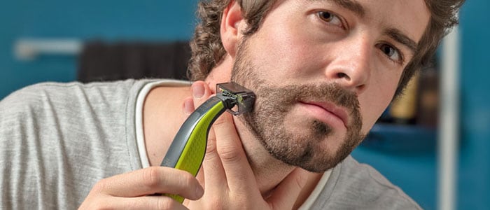 Un uomo rifinisce la barba usando un rasoio con un accessorio speciale. 