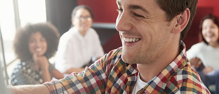 Primo piano del volto di un uomo sorridente, con quattro persone sfocate sullo sfondo.