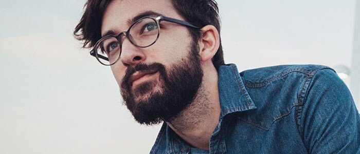 Un uomo dai capelli scuri e barba folta indossa una camicia di jeans.