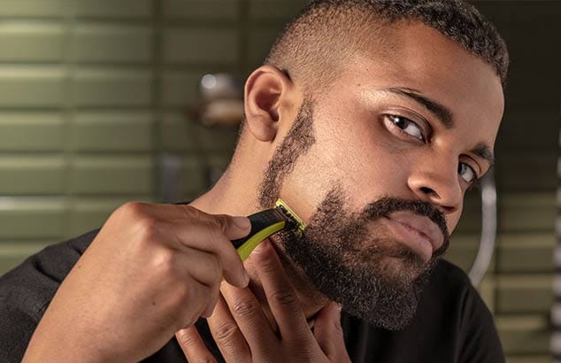 Primo piano di un uomo che si rade la barba corta verticalmente, lasciando una striscia ben rasata sulla guancia.