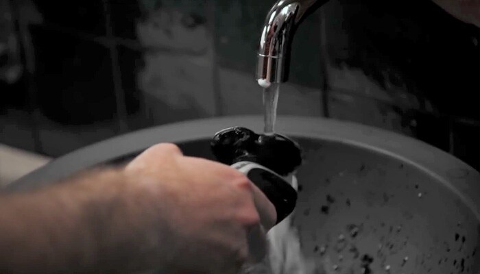 primo piano di un uomo che sciacqua un rasoio elettrico sotto l’acqua corrente per pulirlo