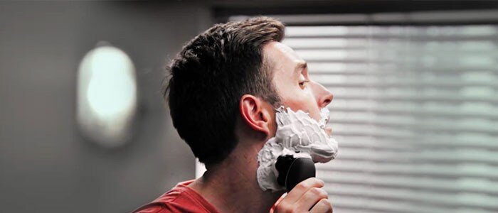 Un uomo con la schiuma da barba sul viso si rade con un rasoio elettrico.